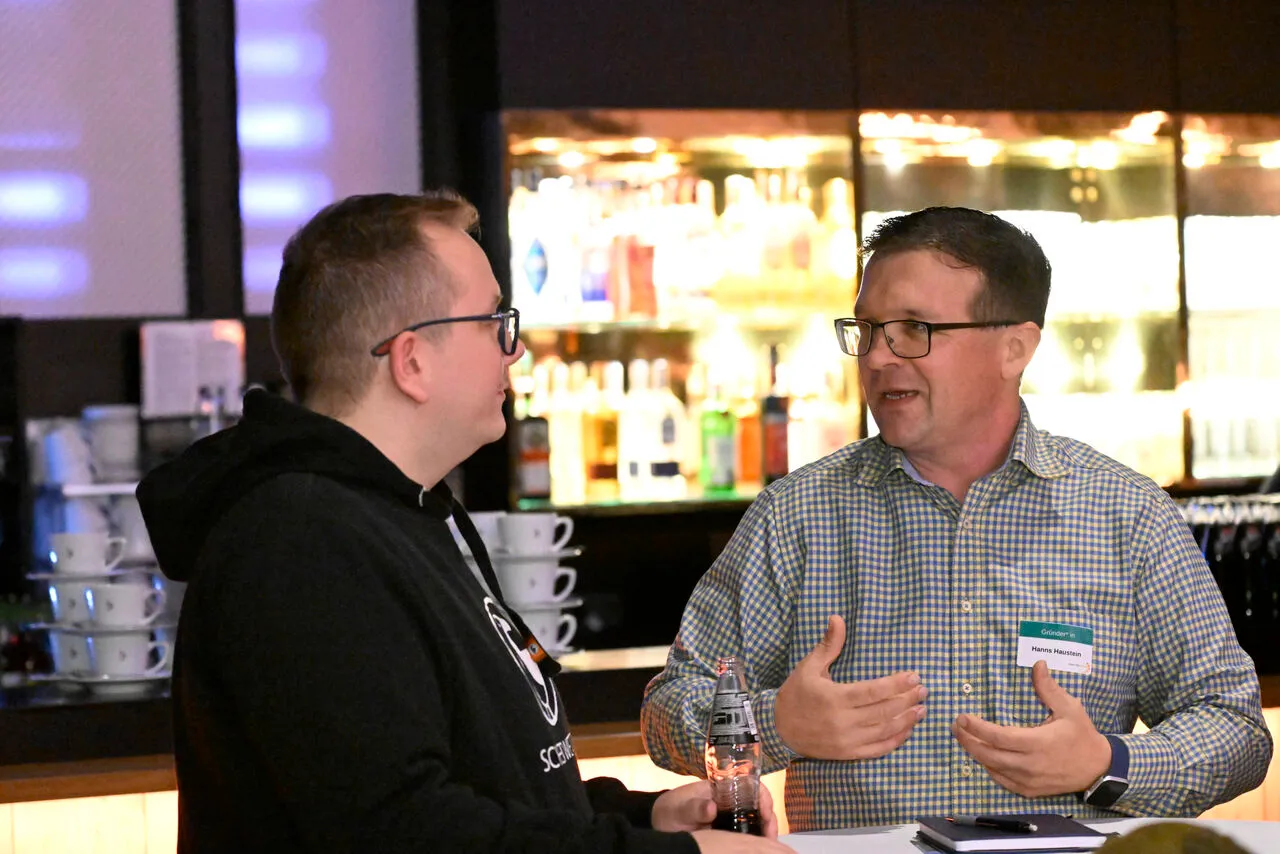 Hanns Haustein in conversation with a coach during a start2grow speed-dating session, wearing a founder name badge.